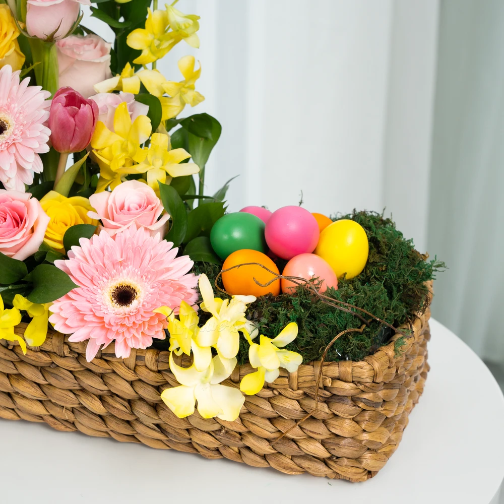 A basket arrangement of 3 pink gerberas, 15 pink roses, 5 yellow roses, 10 pink tulips and 5 stems of yellow orchids with green fillers and multi-colored easter eggs.