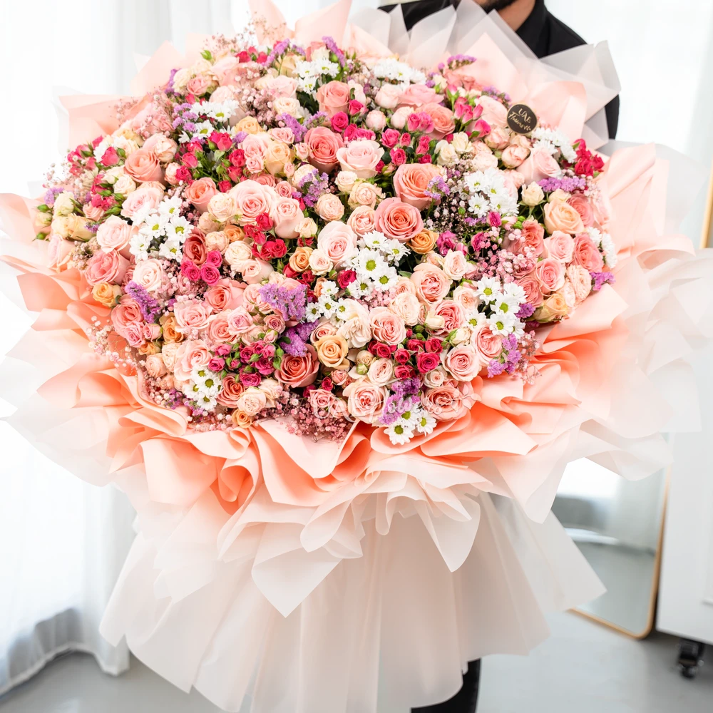 Grand bouquet of 70 mix color spray roses, 80 mix color roses and 10 white chrysanthemum with fillers in paper packing.