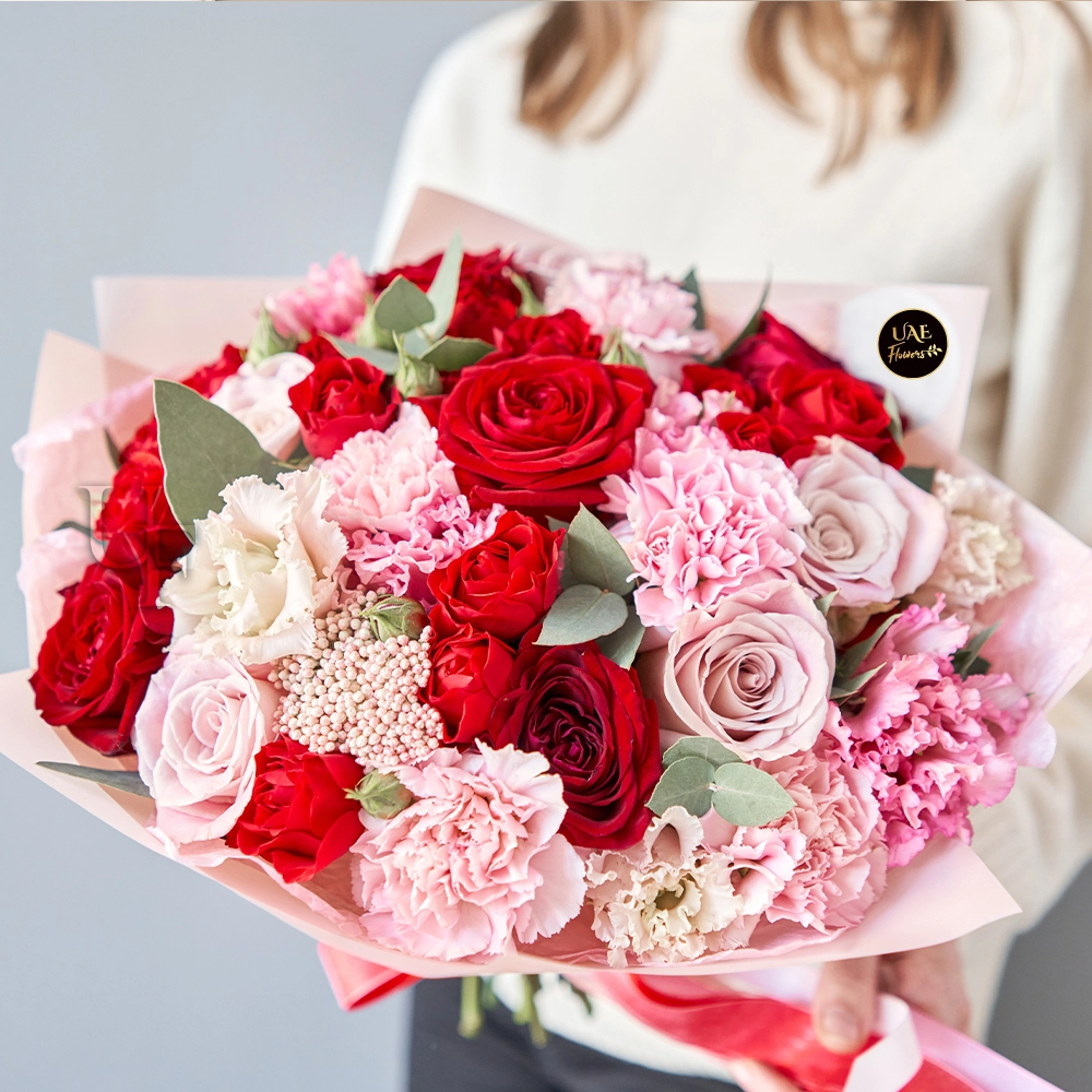 A bouquet containing 25 red and pink roses, 15 pink and white carnations with fillers, wrapped in pink paper, and tied with a red ribbon