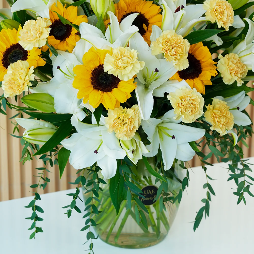 15 white lilies, 10 sunflowers & 20 peach carnations in a glass vase
