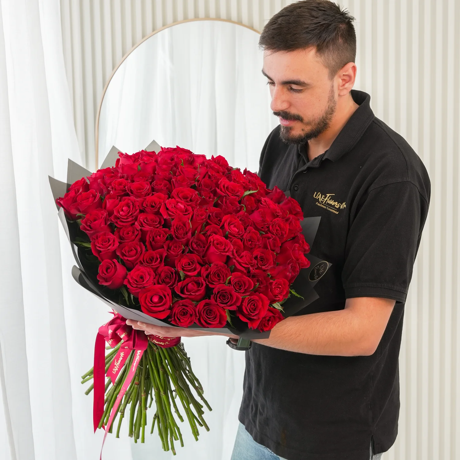 100 premium red roses hand-tied with green fillers and wrapped in black paper with satin ribbon
