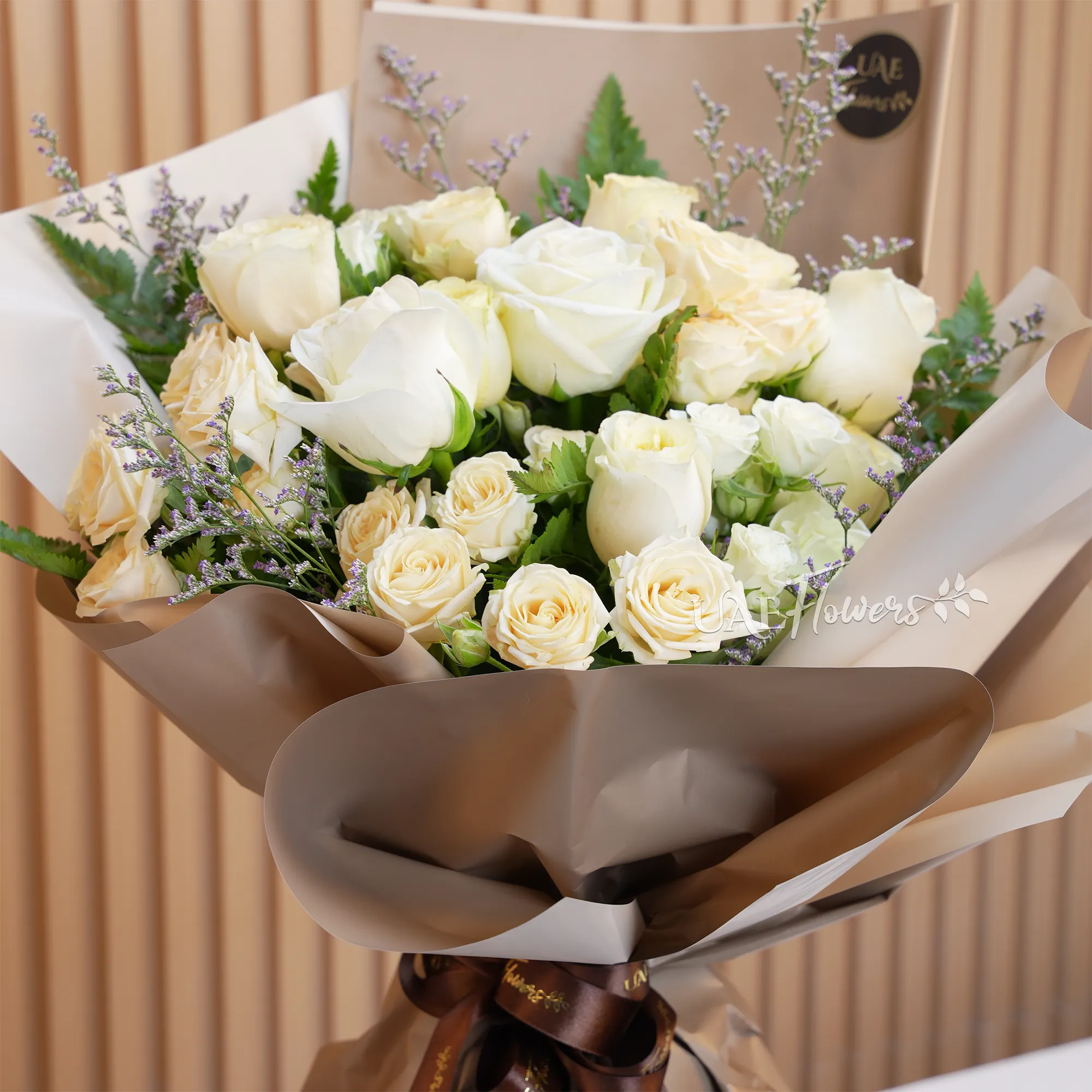 Bouquet of 8 white and peach roses with 2 peach spray roses and green fillers, wrapped in paper and tied with ribbons.