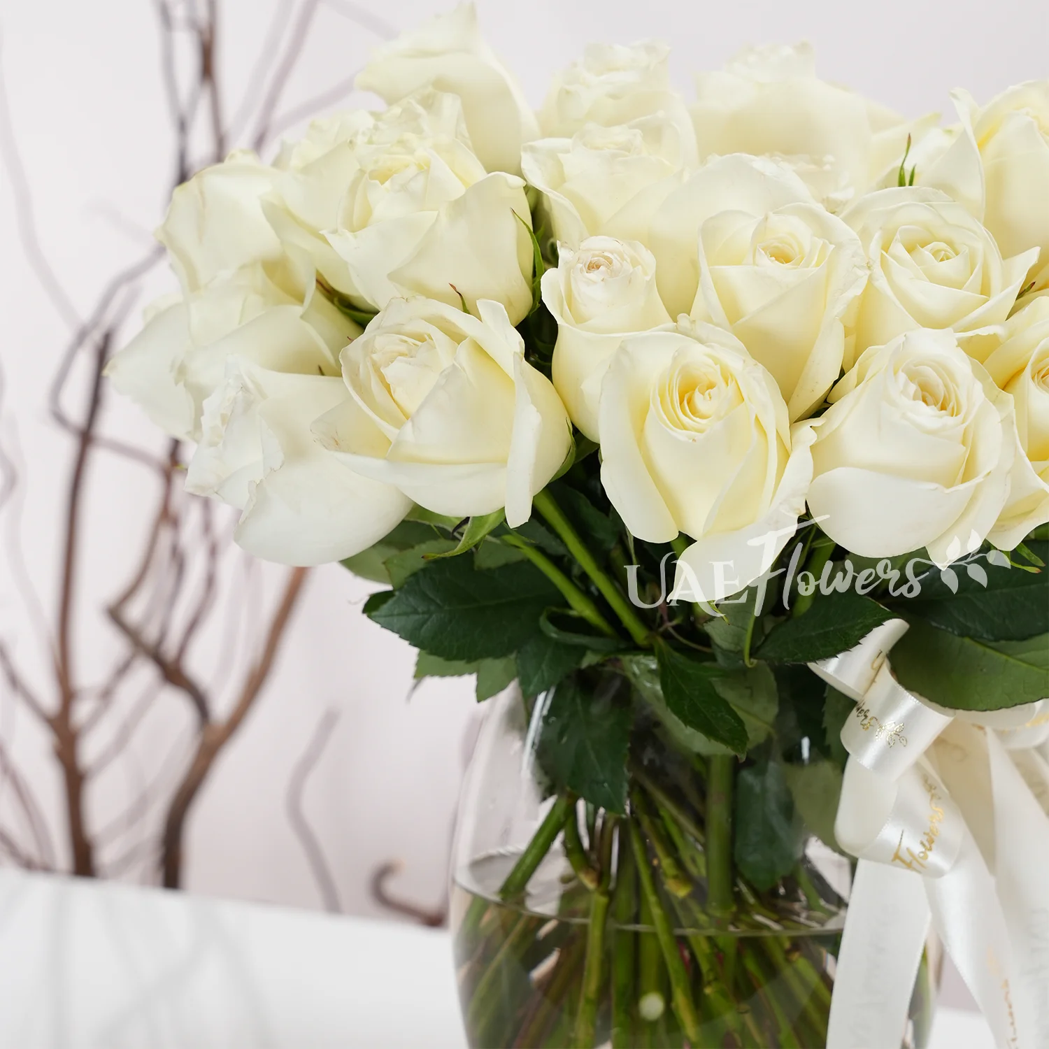 Glass vase with 40 white roses, green fillers, and a delicate white ribbon.
