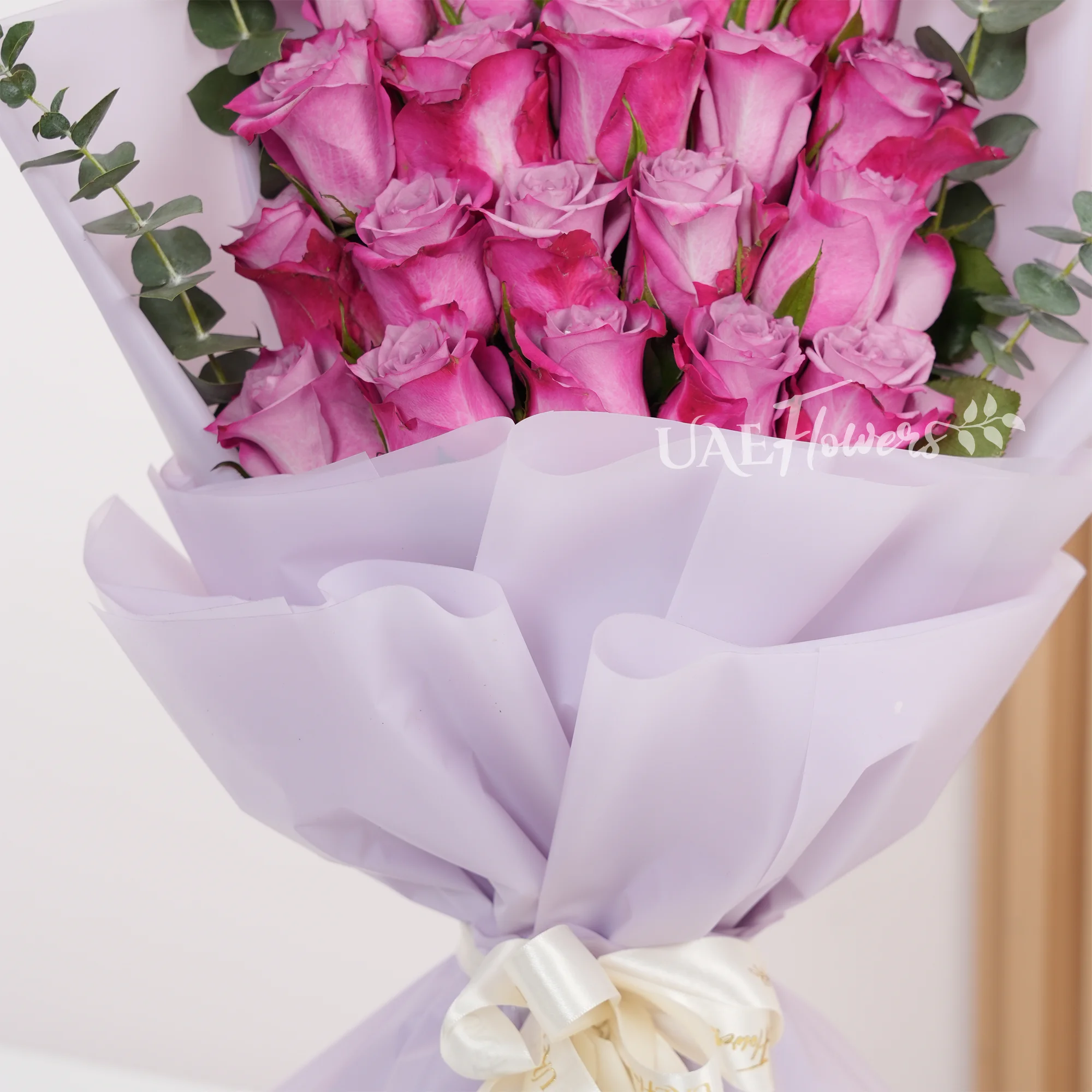 Bouquet of 20 purple roses with eucalyptus leaves, wrapped in pink paper and tied with a white satin ribbon, perfect for gifting and celebrations.