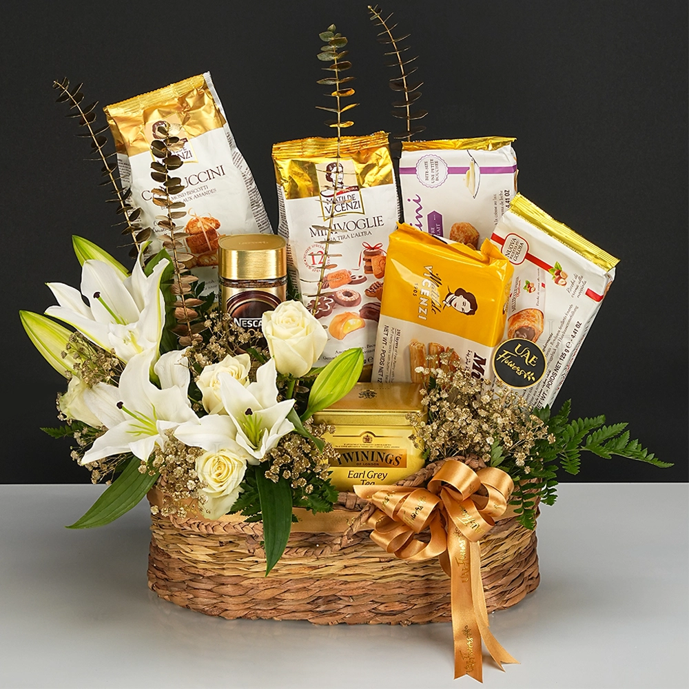 Gourmet gift hamper with Twinings tea, Vicenzi treats, Nescafe coffee, white lilies, and roses, elegantly wrapped with a satin ribbon—ideal for thoughtful gifting.