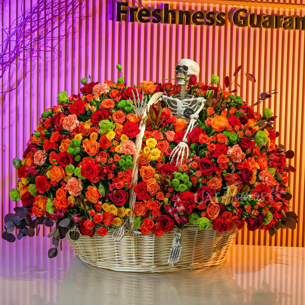 Round basket with orange and yellow spray roses, red roses, carnations, chrysanthemums, and Alstroemeria arranged with ribbons